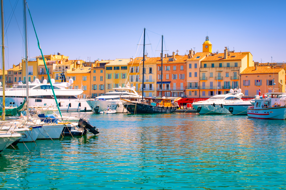 Yachts in St Tropez port with colourful buildings in the background on a clear day