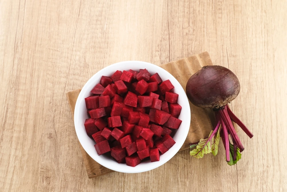 A bowl of Beetroot chunks next to a whole beetroot on a chopping board.