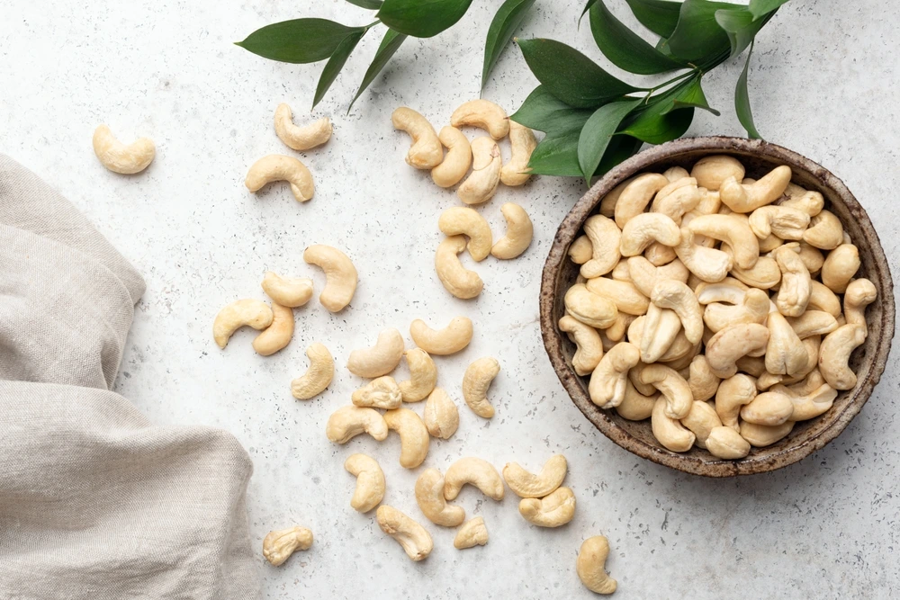 Cashew nuts in a grey bowl next to some spilt cashews on the floor.