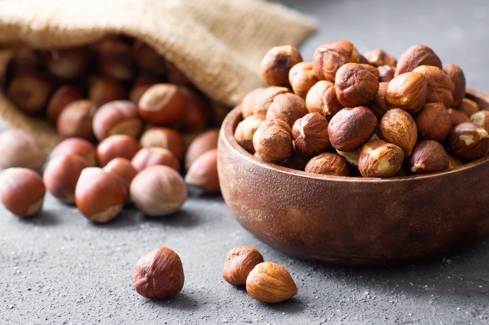 Hazelnuts in a brown bowl next to a sack of hazelnuts that have spilt.