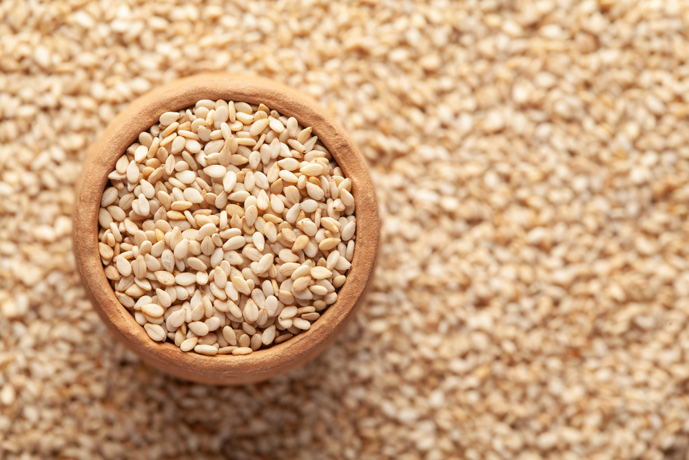 Sesame seeds filling a clay bowl with seeds all over the background.