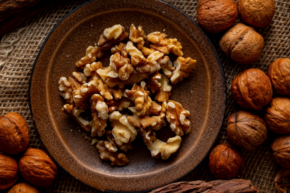 A brown bowl filled with candied walnuts surrounded by whole walnuts.