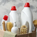 Three bottles of cleaning supplies with brushes and scrubs in a wooden basket.