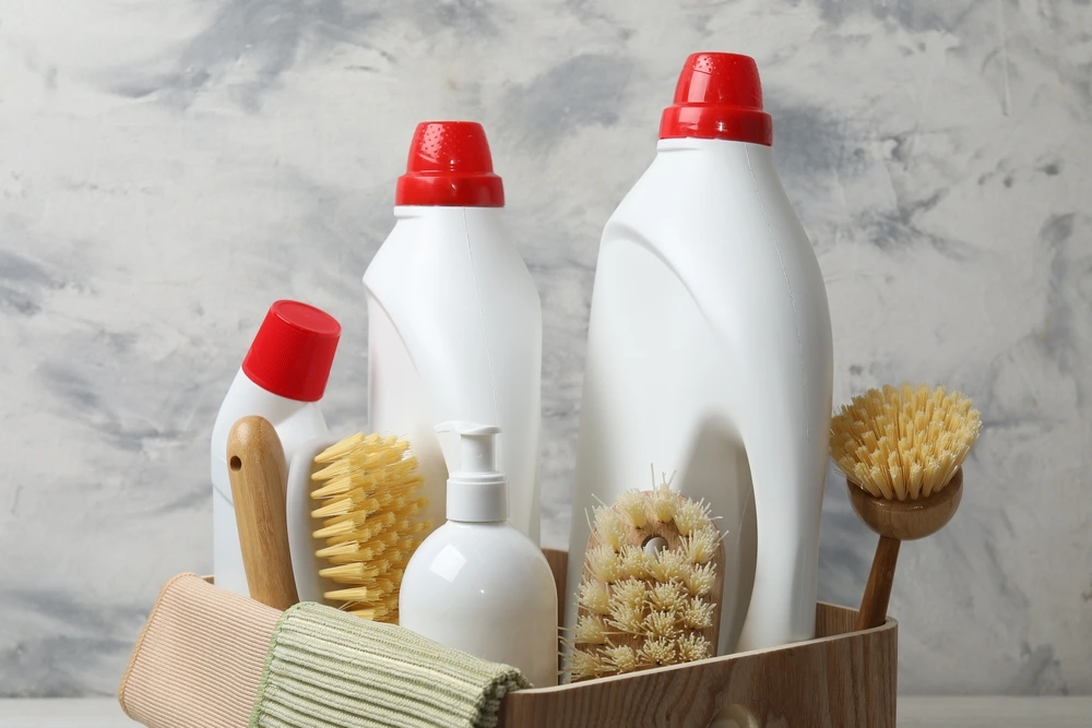 Three bottles of cleaning supplies with brushes and scrubs in a wooden basket.