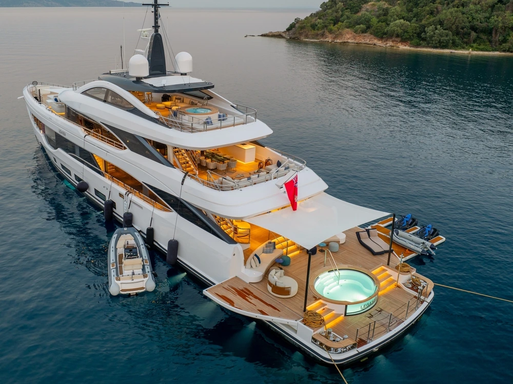The back of a yacht with a jacuzzi on the deck. Lights are on inside as it gets dark.