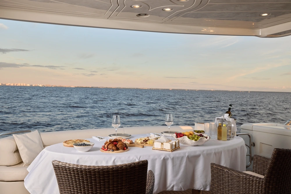Pastries and fruit are on the yacht exterior table with two wine glasses looking out over the horizon.